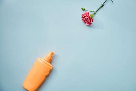 Cosmetic bottle mock up and pink delicate flower on blue background. A modern conceptual female...