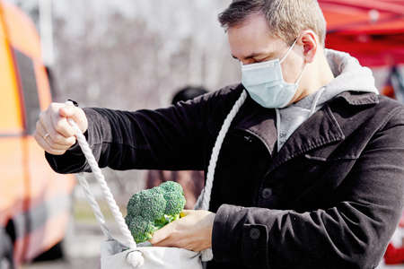 Masked man in the local market buying broccoli cabbage in period of pandemic.