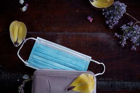 Women clutch explosion with protective mask, lilac flower and yellow tulip petals. Top view. Modern...