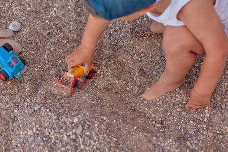 Lovely caucasian child plays with toys in the gravel on the coast near the sea. Summer holiday, fun and vacations concept. High quality photoの写真素材