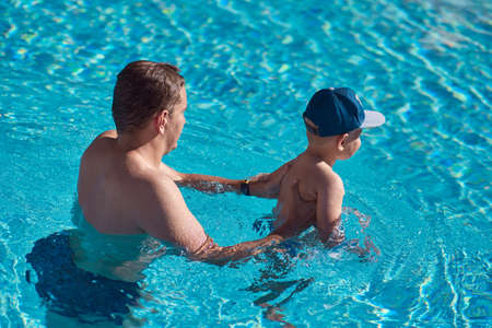 Caucasian father and son in the pool. Father teaches his son to swim in the pool on a sunny day. Hanging out together. Summer fun. High quality photoの写真素材