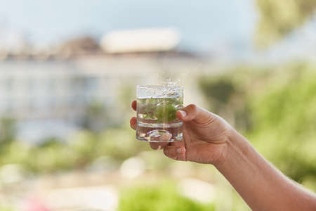 Man holds in his hands a glass of homemade cocktail with antioxidant herbs in front of mountains. summer wallpaper close up.の写真素材
