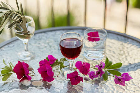 Summer cocktails and elegant glass of red wine. Decorative pink flowers and a branch of an olive tree in a glass. Glyph of Purification. Top view, copy space.の写真素材