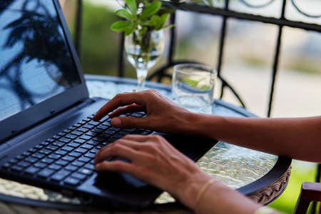 Hands on laptop works by freelance on the terrace on a sunny day. Writing, taking notes, watching...