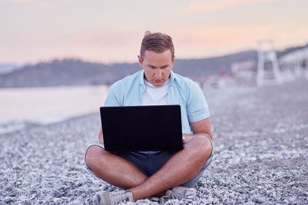 Man brunette with a laptop on a on the beach. Freelancer, working remotely, webinar, learning concept, chatting with friends. New normal conceptの写真素材