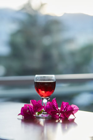 Glass of red wine on blurred mountain background. Decorations of pink bougainvillea flowers. Blue hour photography. Copy space.の写真素材