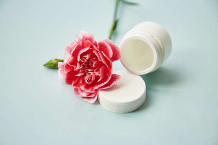 Minimalistic cosmetic bottles mock up with pink decoration flower. Beauty products on blue...