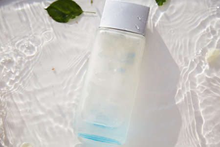 Perfume glass transparent bottle mock up in the water with petals and leaves of white rose. High angle shadows. Top view. Place for text. High quality photoのeditorial素材
