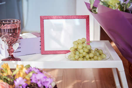 Pink bright frame mock up with sunlight, wineglass with white roses, flowers and grapes. Cozy home. High quality photoのeditorial素材
