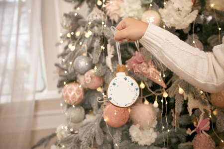 Kid decorates Christmas tree with gingerbread at home. Happy, warm lifestyle. Winter comfort. New...