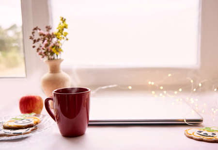 Home office concept in Halloween : laptop and red cup, apple, homemade cookies in shape of cute pumpkins and ghost. Atmospheric working autumn mood. Close upの写真素材
