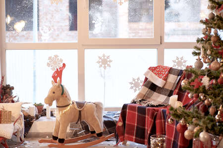Home cozy Christmas decorations. Cozy sofa with plaid and baby horse rocking chair with decorated Christmas tree with gifts near the window. High quality photoの写真素材