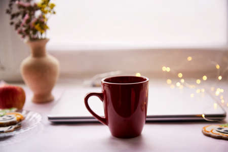 Cozy home office in Halloween : laptop and red cup, homemade cookies in shape of cute pumpkins. Atmospheric working atmosphere with garlands. Copy space.の写真素材