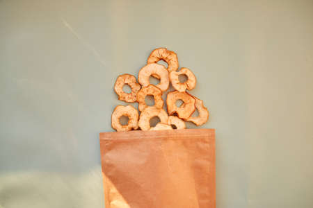 Paper bag with dried sliced apple rings - healthy trendy snacks with modern shades. Top view. Proper...