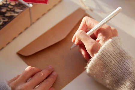 Female hand signs a festive envelope. Preparing for the Christmas holidays. Christmas decorations at...