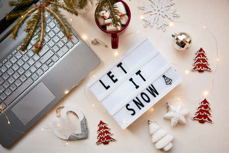 Christmas office atmosphere: laptop, earphones, cozy decorations, cookies, cup of hot beverage, marshmallows and text Let it snow. Top view. Festive holidays at work or remote work, freelance concept.の写真素材