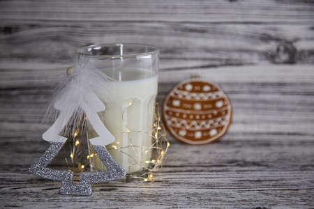 Cute Christmas tradition. Handmade fresh cookies and warm glass of milk on the wooden table. Table setting. Festive Christmas mood and aesthetic atmosphere with garlands. Copy space.の写真素材