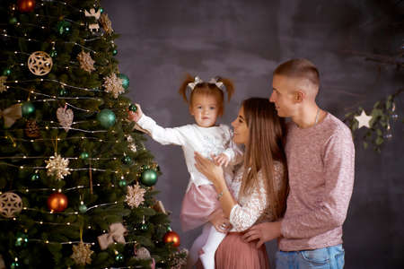 Young family with little baby girl in cozy home interior with festive Christmas tree. Good mood and having fun together. Merry Christmas concept. Happy parenthood concept, true moment.の写真素材