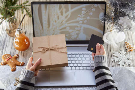 Woman searching and buying Christmas holidays gift online by laptop. Christmas decorations arrangement. Mock up screen. Hot beverage gingerbread in office. Cozy festive workplace. Boxing Day concept.の写真素材