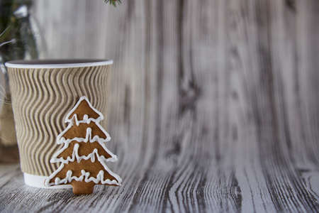 Beige cardboard cup with hot beverage and cookie in shape of Christmas tree. Wooden organic festive Christmas background. Aesthetic cozy home or office concept. Copy spaceの写真素材