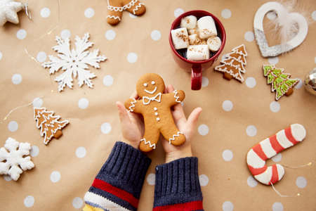 Christmas homemade gingerbread cookies in child hands among festive Christmas decorations with hot drink and marsmallows. Aesthetic Christmas atmosphere, home coziness and warmth conceptの写真素材