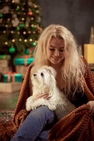 Portrait of cute cheerful girl with their pet white lap dog in aesthetic atmosphere of Christmas...