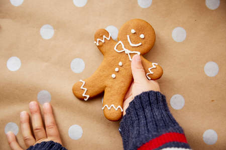 Child holds homemade gingerbread cookie on basic dots background. Festive Christmas atmosphere, home...
