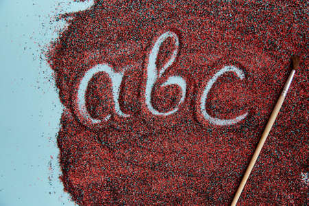 Abstract creative abc handwritten text on red sand surface with paint brush. Top view. Colorful sandの写真素材