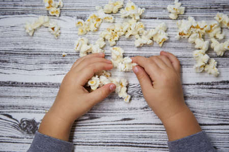 Toddler hands try a popcorn. Kid's curiosity. National Popcorn Day concept. Top view