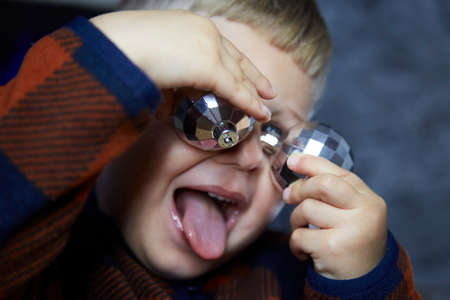 Funny joyful child licks a disco ball. Boy plays with Christmas tree disco ball among Christmas decorations. Festive atmospheric home for New Years Eve. Aesthetic cozy home. Happy baby boyの写真素材