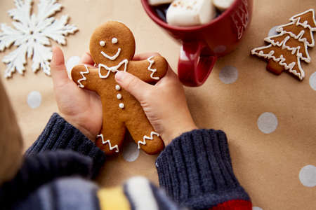 Christmas homemade gingerbread cookies in child hands among festive Christmas decorations with hot drink and marsmallows. Aesthetic Christmas atmosphere, home coziness and warmth conceptの写真素材