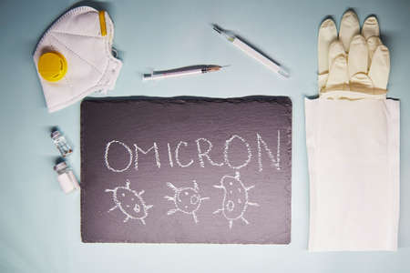 New Variant of the Covid-19 Omicron B.1.1.529 text. Face mask, vaccine, gloves, syringe and thermometer. Omicron variant of coronavirus. Chalk text on blackboard.の写真素材