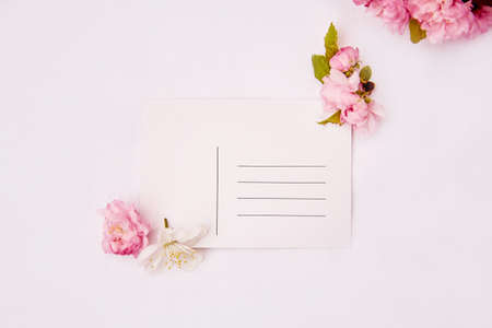 Feminine minimalistic spring pink and white flowers with post card and place for address mock up. Invitation, romantic, wedding, birthday, mothers day card concept. Copy space. Top view.の写真素材