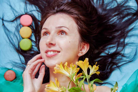 Young woman face close up with flowers and french macarons close up. National Macaroon Day concept....