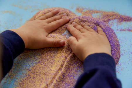 Baby hands play with colorful sand. Child fine motor skills development. Creative kids occupation....