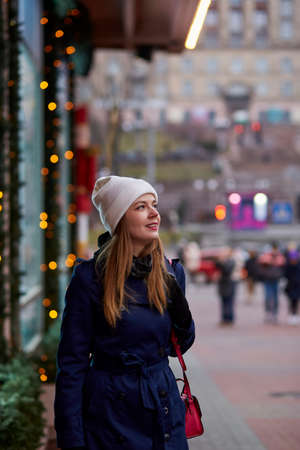 Beautiful caucasian woman in the street near decorated showcase. Stylish winter casual clothes. festival city. city evening lightsの写真素材