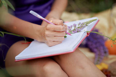 Woman writing in notebook with bouquet of wildflowers - lupines. Closeness to nature, self-discovery...
