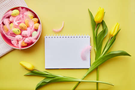 Easter mock up notepad. Pink bright bowl with colorful eggs, pink feathers and yellow tulips. Happy...