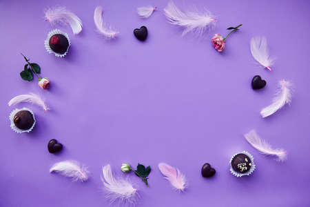 Chocolate and heart shaped candies on purple background. Trendy pink feathers, pink roses. Very peri...