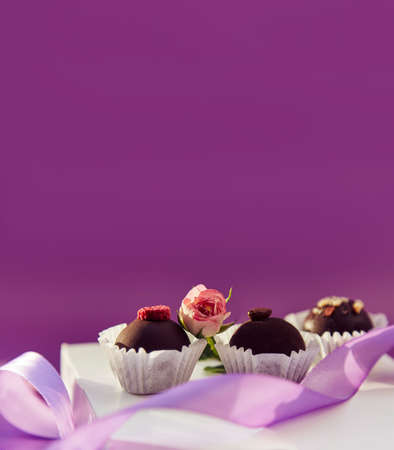 Festive chocolate sweets. Delicate pink feathers and purple ribbon. Purple color pattern with copy...
