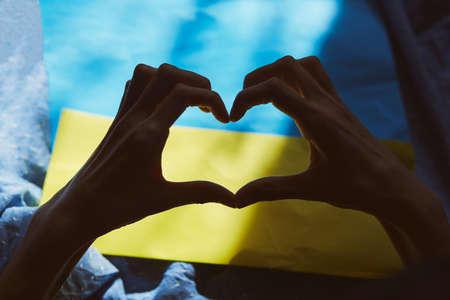 Heart shaped hands on Ukrainian flag with shadows. Priority question. Breaking news. Ukrainian flag,...