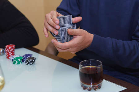 Man's hands shuffle cards in a poker game. Chips, cards, glass of whiskey on the table with reflection. poker club.の写真素材