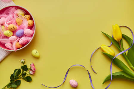 Easter bright background. Pink bowl with colorful eggs, pink feathers, spring flowers. Happy Easter...