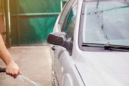 Man washing the car with water with the hose in the private yard. Spring cleaning concept. caring...