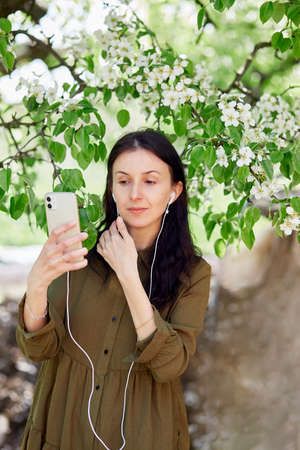Young woman surfing in phone and using headphones, listen to music, online meeting or chatting with friends. Taking webinar lesson, listen online course, learn language in app. Relaxing and leisure.の写真素材