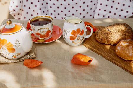 Summer traditional poppy seed bun with cup of tea and milk near poppies flowers and dishes with...
