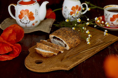 Traditional poppy seed buns, cup of black tea and milk among poppies flowers and dishes with poppies...