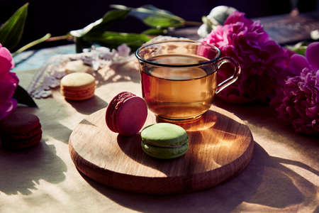 Herbal tea and macarons dessert for brunch outside in the terrace. Blooming pink peony flowers under trendy hard shadows. Relaxation, thoughtful, meditative, good mood lifestyleの写真素材