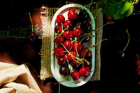 Fresh cherry in the plate on black background under hard shadows. Rustic natural home-grown berries....
