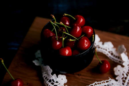 Fresh cherry in glass bowl on the sacking on black background in a low key with lace decoration....